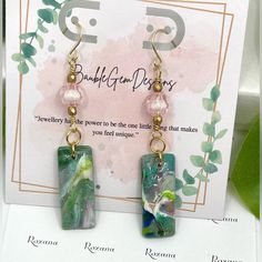 a pair of earrings with green and blue designs on them sitting on top of a card