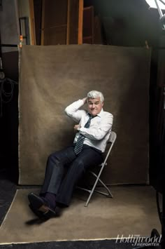 an older man sitting in a chair with his hands on his head while posing for a photo