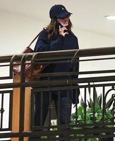 a woman standing on top of a balcony talking on a cell phone while holding a purse