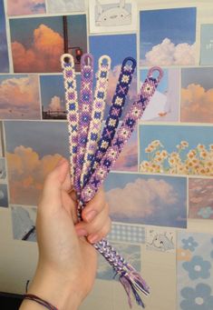 a person holding up some beads in front of a wall with pictures and flowers on it