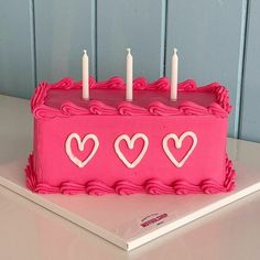 a pink birthday cake with hearts and candles on the top is sitting on a table