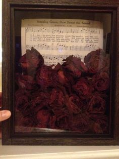 someone is holding up a framed photo with sheet music and flowers in the frame,