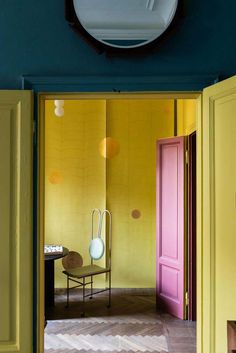 a room with yellow walls and pink doors, an oval mirror on the wall above it