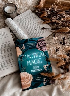 an open book sitting on top of a bed next to two candles and some dried flowers