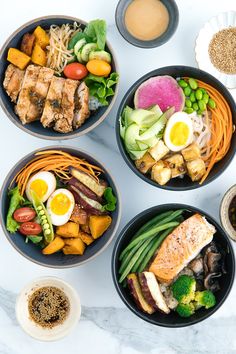 four bowls filled with different types of food on top of a white table next to bottles of ketchup