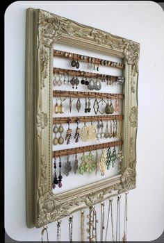 an ornate frame holds several pairs of earrings and earring hooks on a white wall