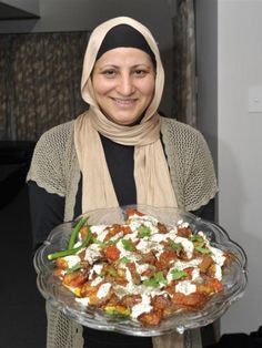 a woman in hijab holding a platter of food with vegetables on it