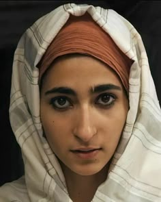 a woman wearing a white and orange head scarf on top of her head is looking at the camera