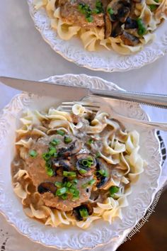 two plates with pasta, mushrooms and peas on them next to a knife and fork