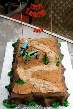 a birthday cake that is shaped like a dirt track with a car on it and two flags