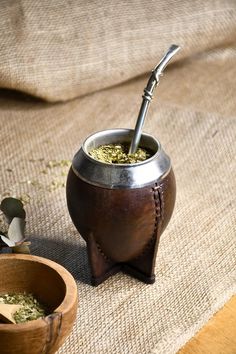 a wooden bowl filled with green tea next to a small metal cup on top of a table