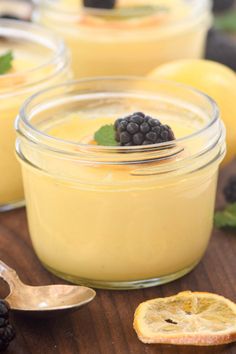 three small jars filled with pudding on top of a wooden table next to blackberries