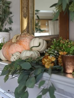 a fireplace mantel decorated with white pumpkins and greenery