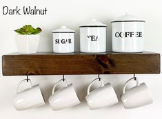 three white coffee mugs are hanging on a wooden shelf with two pots and one plant