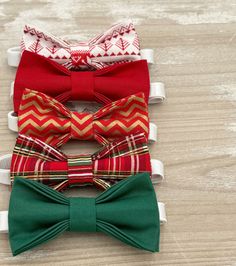 four bow ties are lined up on a wooden surface, one is red and the other is green