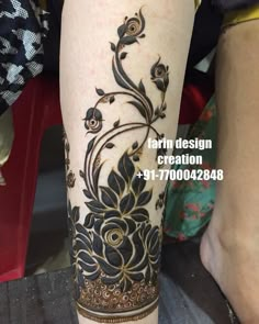 a woman's leg is decorated with black and gold flowers, leaves and scrolls