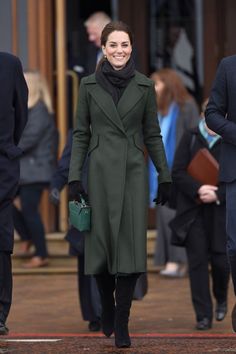 a woman in a green coat and black gloves is walking down the street with other people