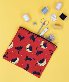 a red pouch with black cats and moon on it next to scissors, sprinkles, and other items