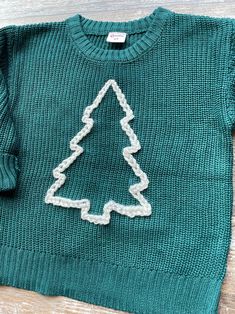 a green sweater with a white christmas tree on the front and bottom, sitting on a wooden surface