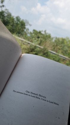 an open book sitting on top of a window sill next to a lush green forest