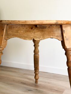 an old wooden table sitting on top of a hard wood floor next to a white wall