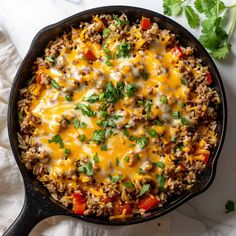 a skillet filled with ground beef and rice topped with cilantro, red peppers, and parsley