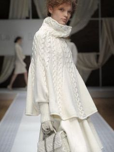 a woman is walking down the runway wearing a white sweater