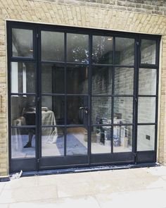 an open glass door on the side of a brick building that has been painted black