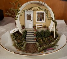 a plate with a miniature house on it and plants growing out of the front door