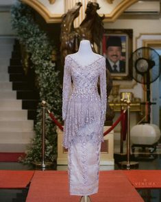 a dress is on display in front of a painting and stairs with red carpeting