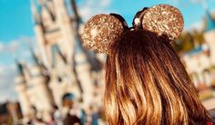 the back of a woman's head with ears in front of a disney castle