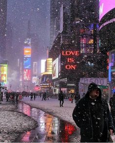 people walking in the snow on a city street at night with neon signs and buildings