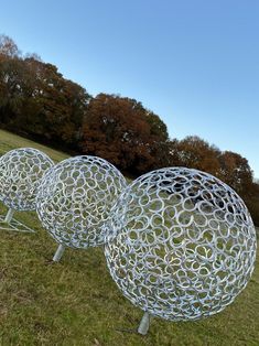 three large metal balls sitting on top of a grass covered field next to each other