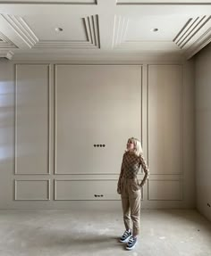 a woman standing in an empty room with white walls and ceiling tiles on the floor