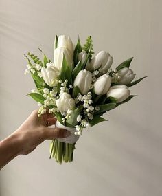 a bouquet of white tulips and lily of the valley in someone's hand