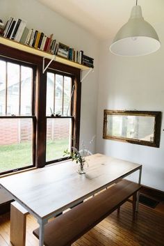 a dining room table in front of two windows with bookshelves on the wall