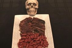 a skull is sitting next to a plate of meat and sausages on a table