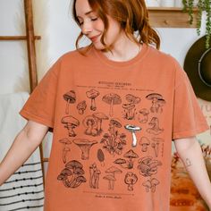 Mycologic Specimens t-shirt designed by Linden & Lichen Studio. The soft vintage wash tee features a variety of vintage mushroom illustrations. Also available in a Comfort Colors sweatshirt! Printed in and shipped from the U.S. Comfort Colors introduces its garment-dyed t-shirt 100% with ring-spun cotton. The soft-washed, garment-dyed fabric brings extra coziness to your wardrobe while the relaxed fit makes it an excellent daily choice. The double-needle stitching throughout the tee makes it hig Mushroom Print Graphic Tee With Crew Neck, Mushroom Print Crew Neck Graphic Tee, Short Sleeve Graphic Tee With Mushroom Print, Short Sleeve Mushroom Print Graphic Tee, Casual Short Sleeve T-shirt With Mushroom Print, Short Sleeve Tops With Mushroom Print For Streetwear, Relaxed Fit Short Sleeve Tops With Mushroom Design, Relaxed Fit Tops With Mushroom Print For Streetwear, Relaxed Fit Mushroom Print Top For Streetwear