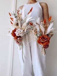 a woman is holding two bouquets of flowers in her hands and wearing white pants