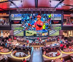 the inside of a sports stadium with people sitting at tables and watching televisions on large screens