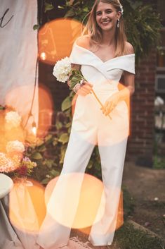 a woman in white jumpsuits standing next to a wall with balloons and flowers