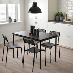 a black table and four chairs in a room with white walls, hardwood floors and windows