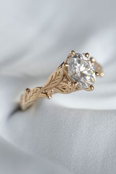 a close up view of a gold ring with a white diamond in the center and leaves on it