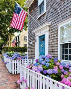 the american flag is flying in front of a house with hydrangeas and bushes