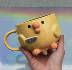 a hand holding a yellow mug with a face on it