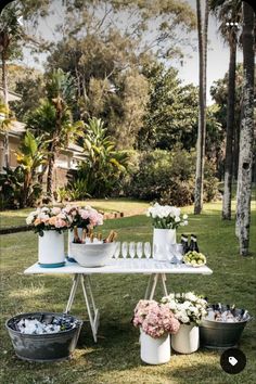 a table with flowers and wine glasses on it in the middle of grass near palm trees