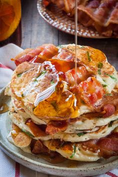 a stack of pancakes with bacon, cheese and syrup being drizzled on top