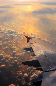 the wing of an airplane as it flies through the sky with clouds and sun in the background