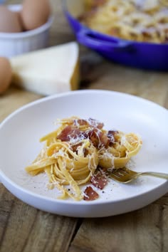 a white plate topped with pasta covered in sauce and bacon next to an egg dish