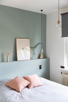 a bed with two pink pillows on top of it next to a wall mounted plant